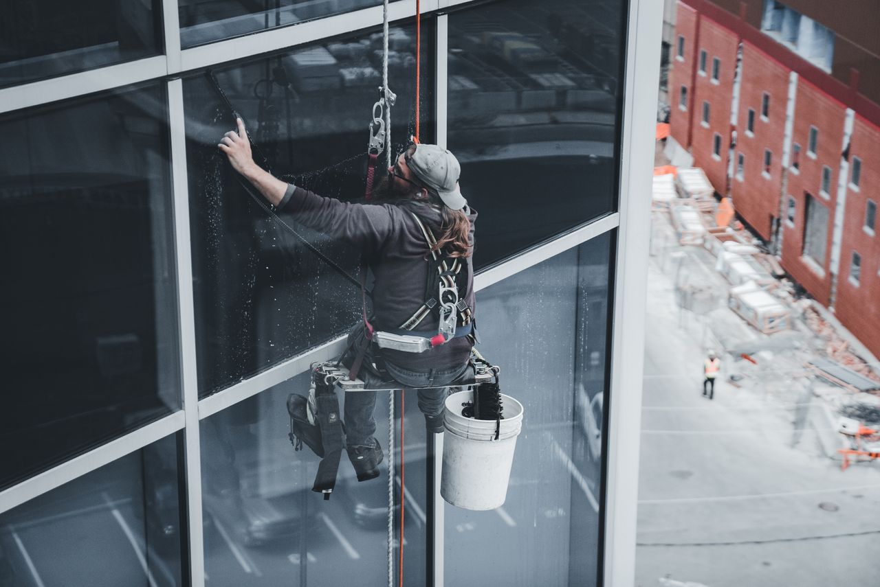 project-01-d A worker cleaning skyscraper windows with a harness in an urban setting.
