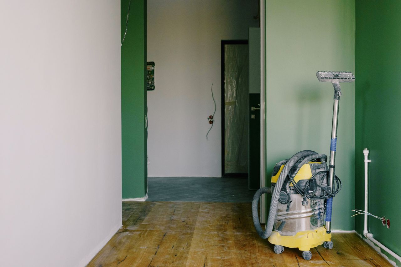 hero-img Industrial vacuum cleaner placed on dirty parquet in room with green walls and doorway in spacious apartment during repair works